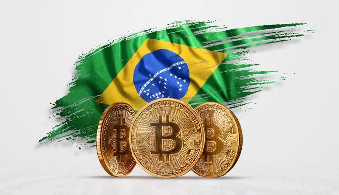 Bandeira do Brasil atrás de moedas físicas do Bitcoin