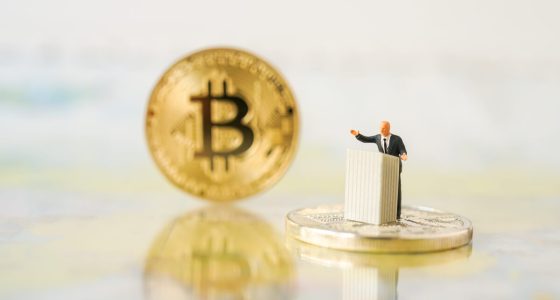 miniatura de homem sob pulpito e moeda gigante de bitcoin ao lado