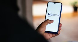 Uma pessoa de costa mexe no celular com logotipo do banco BTG Pactual