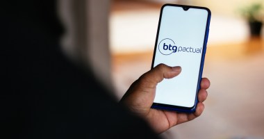 Uma pessoa de costa mexe no celular com logotipo do banco BTG Pactual
