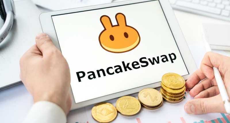 Tela de tablet mostra logotipo da PancakeSwap e moedas douradas aolado