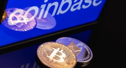 Moeda de bitcoin e etehreum à frente de tela com logo da Coinbase