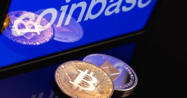 Moeda de bitcoin e etehreum à frente de tela com logo da Coinbase