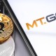 Moeda de bitcoin ao lado de smartphone com logotipo da corretora Mt.Gox