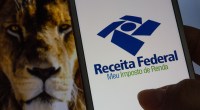 Smartphone mostra logotipo da Receita Federal; ao fundo, um leão