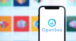 Celular à frente de grande tela de computador mostra logo da Opensea