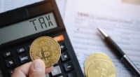 Uma pessoa segura uma moeda de bitcoin na frente de uma calculadora com o termo taxa