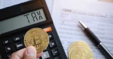 Uma pessoa segura uma moeda de bitcoin na frente de uma calculadora com o termo taxa