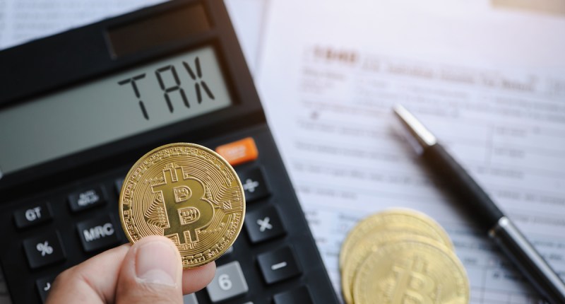 Uma pessoa segura uma moeda de bitcoin na frente de uma calculadora com o termo taxa