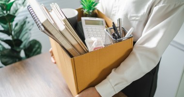 pessoa segura caixa de papelao com seus pertences de escritório após demissao