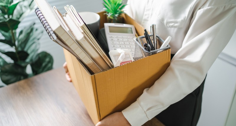 pessoa segura caixa de papelao com seus pertences de escritório após demissao