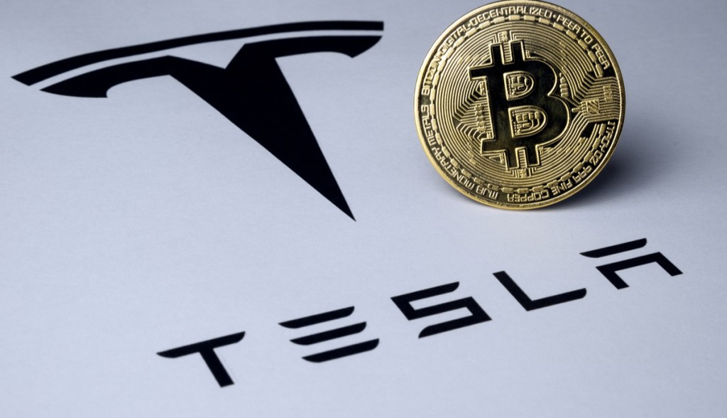 Moeda de Bitcoin sobre logomarca da Tesla