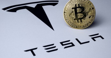 Moeda de Bitcoin sobre logomarca da Tesla