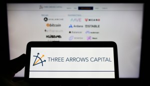 Celular com imagem da Three Arrows Capital na frente dela com logos do bitcoin e criptomoedas