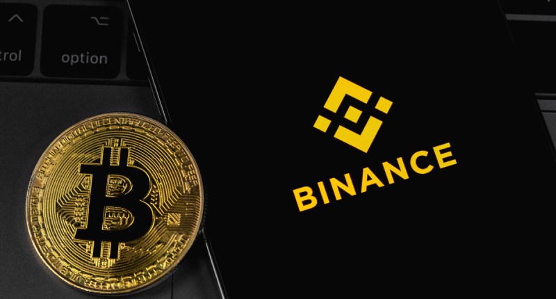 Logo da Binance na tela do smartphone com bitcoin ao lado