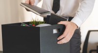 Mão segurando uma caixa cheia de pertences, sugerindo demissão ou renúncia de emprego