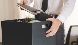 Mão segurando uma caixa cheia de pertences, sugerindo demissão ou renúncia de emprego