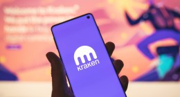 Smartphone com logotipo Kraken na mão com site desfocado como plano de fundo