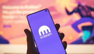 Smartphone com logotipo Kraken na mão com site desfocado como plano de fundo
