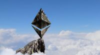Logo do Ethereum é exibido com uma textura de pedra no topo de uma montanha, acima das nuvens