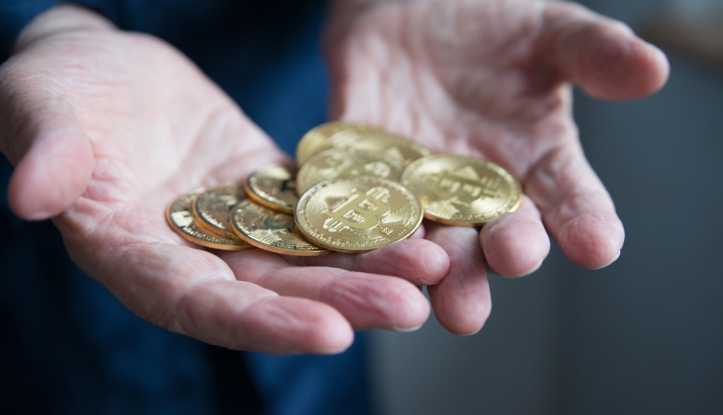 mãos segurando várias moedas de bitcoin
