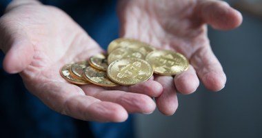 mãos segurando várias moedas de bitcoin