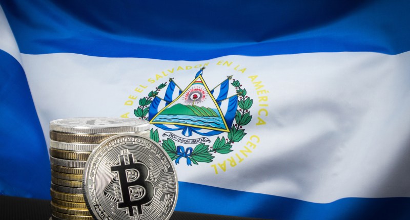Bandeira de El Salvador ao fundo, e moedas de Bitcoin