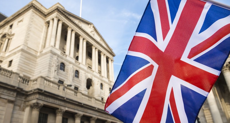 Bandeira do Reino Unido em destaque e o prédio do Banco da Inglaterra em desfoque ao fundo