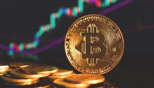 Moedas douradas de Bitcoin (BTC) em frente a um gráfico de preço de alta