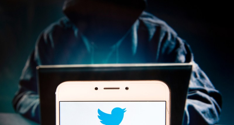 Pessoa encapuzada em um notebook- à frente o logo do Twitter logo do Twitter