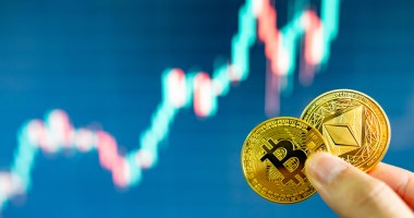 Uma pessoa segura moedas de bitcoin e ethereum - ao fundo um gráfico de mercado de alta