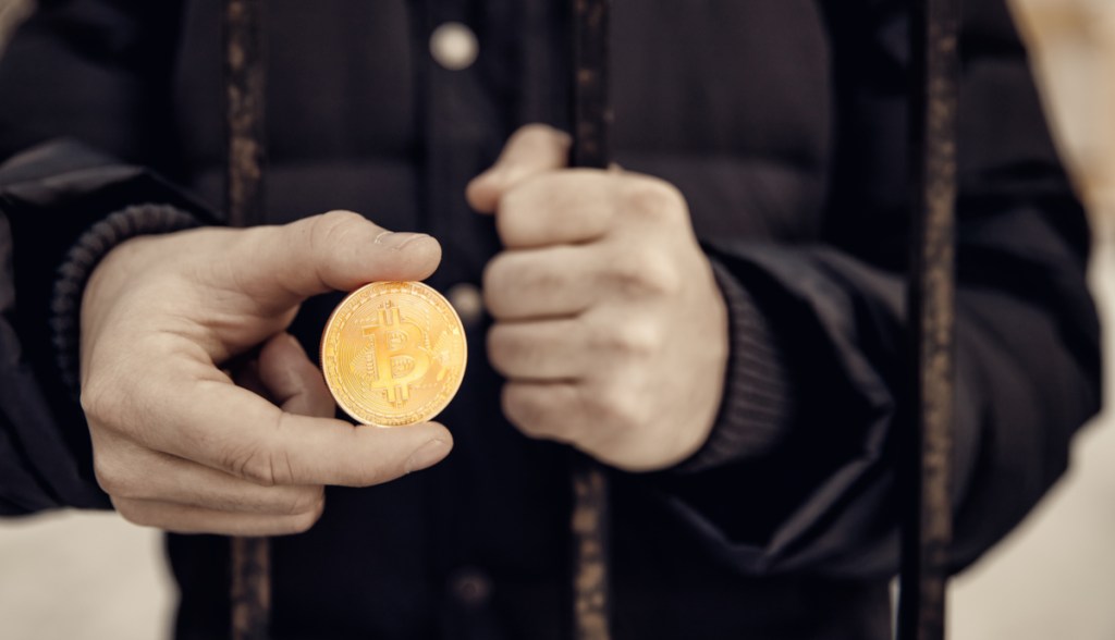 homem preso atrás das grades segurando bitcoin