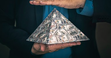 Pirâmide ilustrada com notas de dinheiro sob a mão