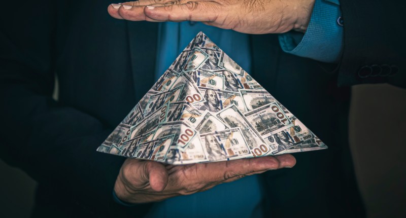Pirâmide ilustrada com notas de dinheiro sob a mão