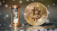 Ampulheta com tempo acabando ao lado de uma moeda de bitcoin