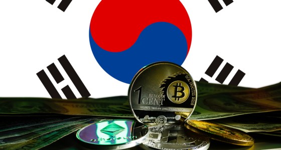 Criptomoedas sobre uma mesa e uma bandeira da Coreia do Sul ao fundo