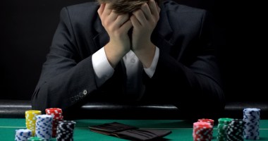 Homem apoia cabeça nas mãos em sinal de desespero-na mesa, uma carteira vazia e fichas de cassino