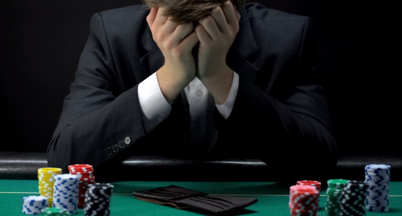 Homem apoia cabeça nas mãos em sinal de desespero-na mesa, uma carteira vazia e fichas de cassino