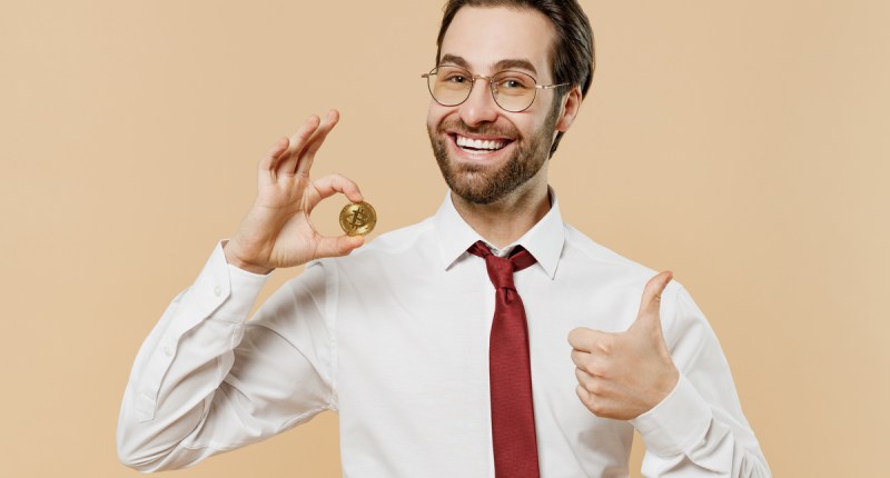 Homem de gravata segura contente uma moeda de bitcoin