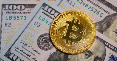 Moeda dourada de Bitcoin (BTC) sobre cédulas de cem dólares