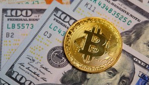 Moeda dourada de Bitcoin (BTC) sobre cédulas de cem dólares