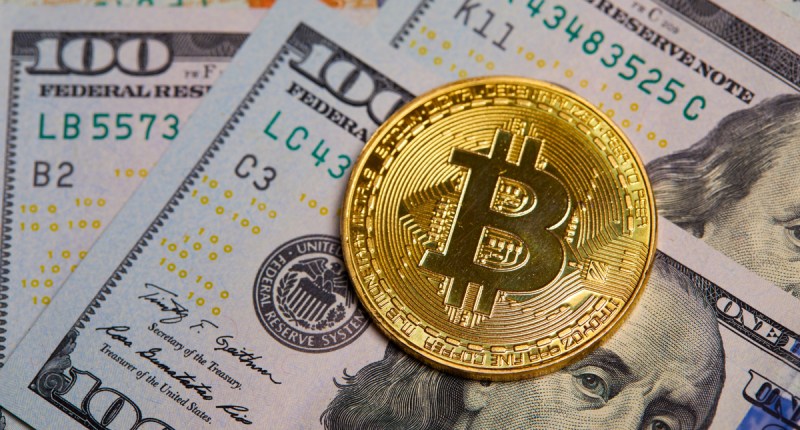 Moeda dourada de Bitcoin (BTC) sobre cédulas de cem dólares