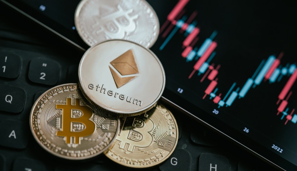 Moedas de Bitcoin (BTC) e Ethereum (ETH) próximas de um gráfico de candles com dados oscilantes de preço