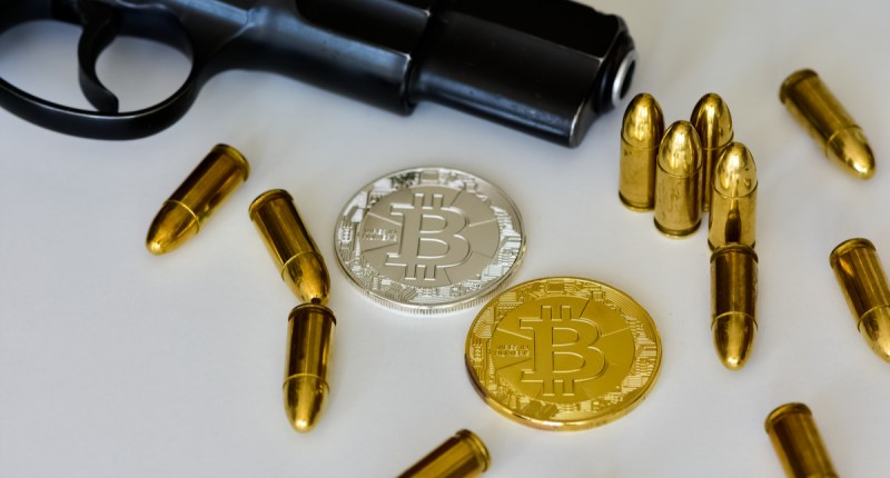 Uma pistola, munições e moeda de bitcoin sobre uma mesa