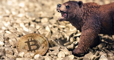 Urso marrom de brinquedo próximo a uma moeda dourada de Bitcoin (BTC), indicando um ciclo de baixa no mercado