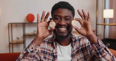 Homem preto sorrindo segura em ambas as mãos moedas de bitcoin