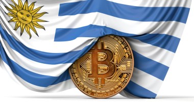 Moeda de bitcoin semicoberta por bandeira nacional do Uruguai