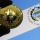 Pessoa segura moeda de bitcoin à frente de bandeira de El Salvador