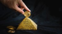 uma pessoa apoia uma moeda de bitcoin no topo de uma maquete de pirâmide dourada