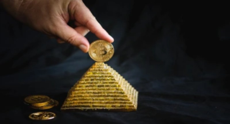 uma pessoa apoia uma moeda de bitcoin no topo de uma maquete de pirâmide dourada